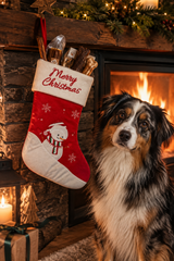 gourmetpfoten.de Weihnachtsstrumpf in Rot mit Schneemann-Stickerei und Merry Christmas Schriftzug neben einem Hund